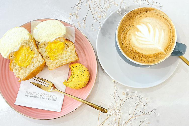 photograph of yellow macaron and cupcake on a pink plate beside a latte 