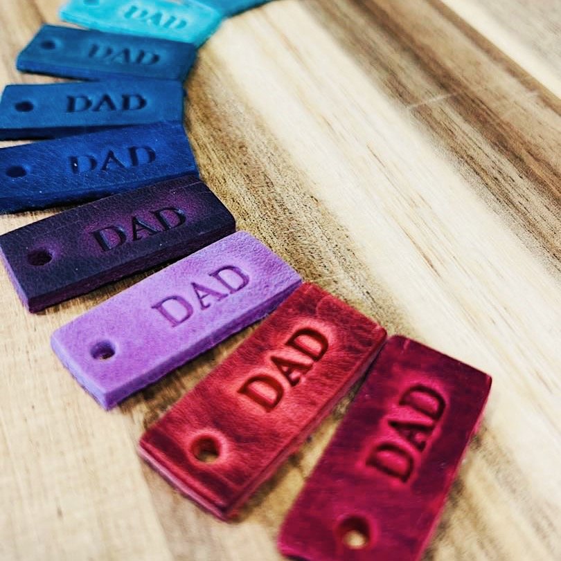 rainbow coloured leather tabs with 'dad' stamped into them on a brown table